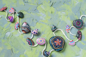 Colorful green and blue textured background with hand-painted acrylic paint stones and shells. Children's art project, a craft for children. DIY concept. Technique dot painting