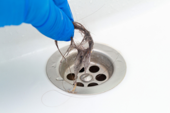 gloved hand pulling hair from drain